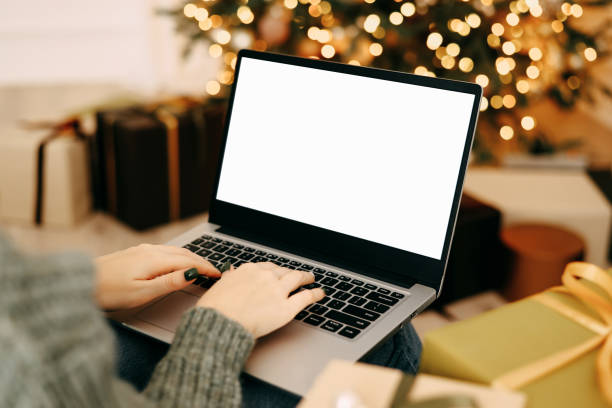 istock woman work on laptop computer with blank display screen with mockup copy space. home interior decorated for Christmas celebration with Christmas tree and garland lights. 1352831060
