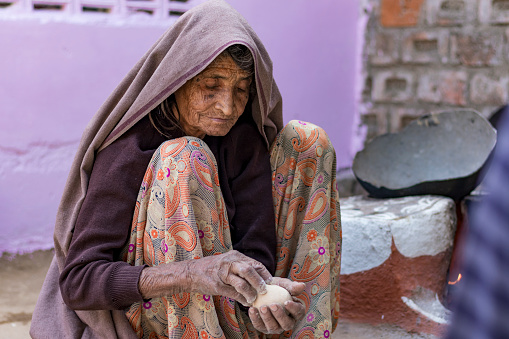 an indian old age woman making food for family in rajasthan, india