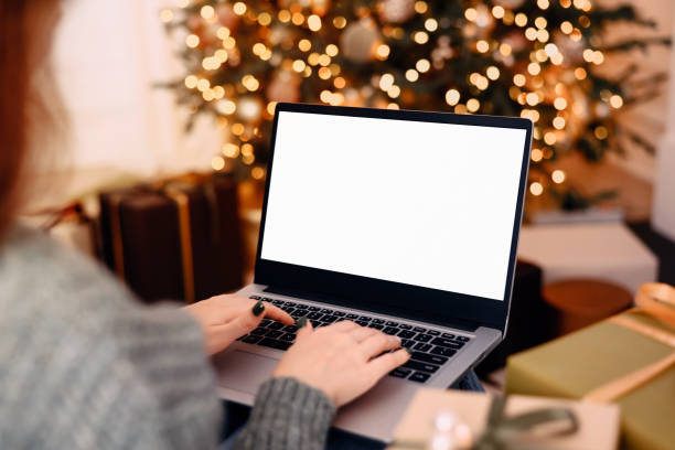 istock woman work on laptop computer with blank display screen with mockup copy space. home interior decorated for Christmas celebration with Christmas tree and garland lights. 1352831841