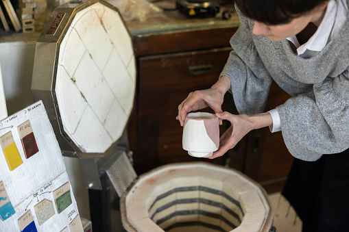 Young Woman Ceramic Artisan in her Studio Workshop putting hr ceramic items into kiln and setting the right temperature for chosen ceramic glaze