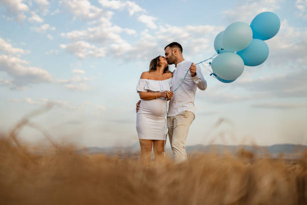 Husband and wife in love revealing baby gender in nature Happy pregnant heterosexual couple in love revealing baby gender with blue balloons in nature on a sunny summer day couple hope sky blue stock pictures, royalty-free photos & images