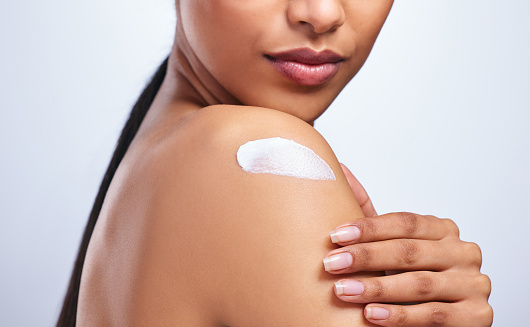 Foto recortada de una mujer irreconocible que se aplica crema hidratante en el hombro sobre un fondo gris photo