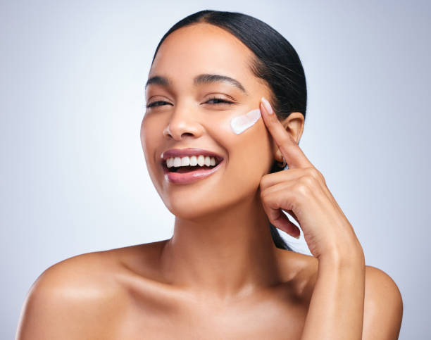 Portrait of an attractive young woman applying moisturiser against a grey background Frantically rebooting my life skin care stock pictures, royalty-free photos & images