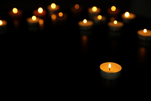 Many burning tealight candles on dark background, space for text