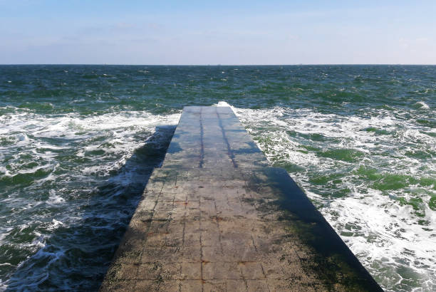 istock A stone breakwater extending into perspective far into the cold winter sea with foamy waves. 1352843260