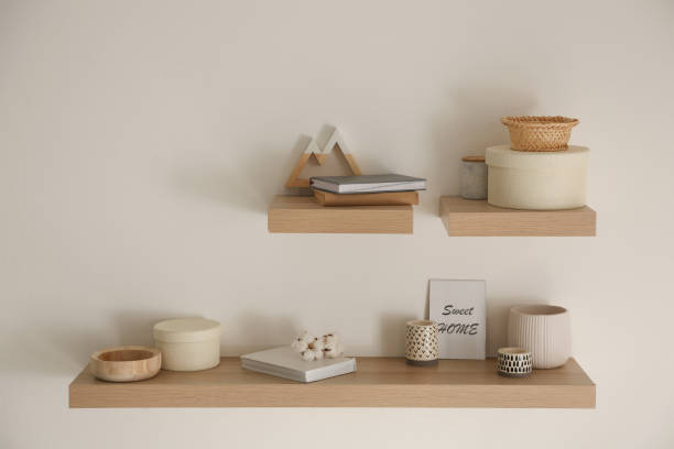 istock Wooden shelves with books and different decorative elements on light wall 1352844166