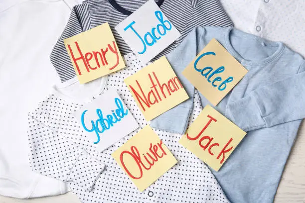 Photo of Many sticky notes with different baby names on child's clothes, flat lay