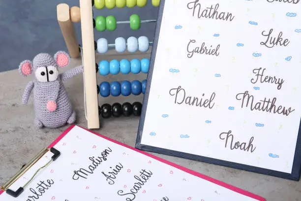 Photo of Clipboard with different baby names and toys on grey table, closeup