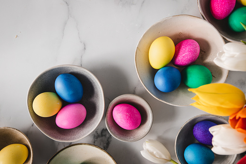Directly above shot of colorful eggs in bowls with tulips flowers over marble surface. Easter decoration background.