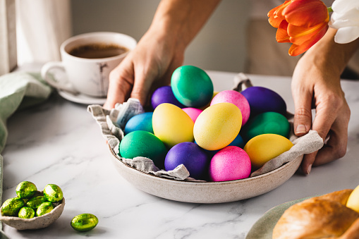 Close-up of a woman arranging colorful Easter eggs plate over breakfast table at home. Female decorating table for Easter breakfast.