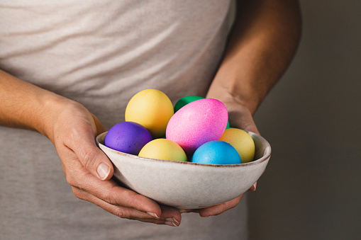 Close-up of a woman hands holding stacked bowls full of pastel colored Easter eggs. Hand holding up a bowl filled with eggs in various colors.
