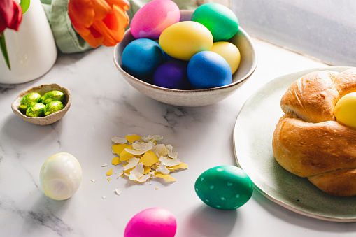 Easter celebration, colorful and decorated eggs on table with crushed egg shells and bread nest on plate.