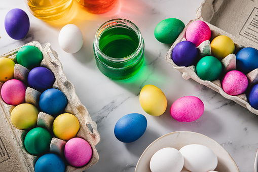 Colorful dye bottles with multicoloed Easter eggs  in cartons over a table. Coloring eggs in bright colors for Easter holiday.