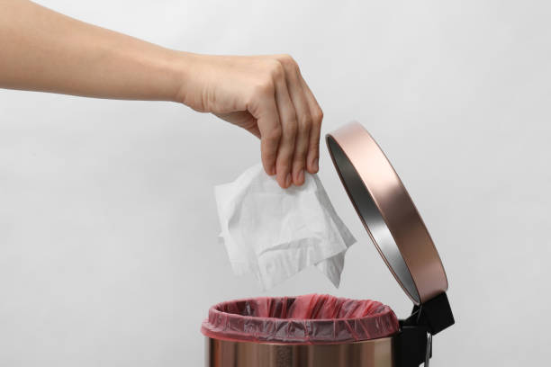 istock Woman putting paper tissue into trash bin on light background, closeup 1352848624