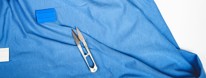 Sewing accessories, scissors and threads on table, top view. Blue fabric cotton jersey