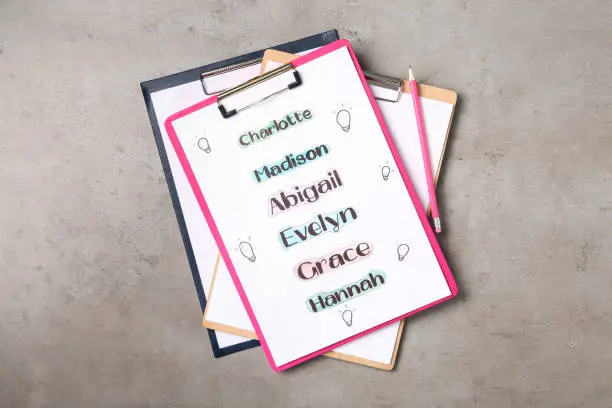 Photo of Clipboards with different baby names and pencil on grey table, top view