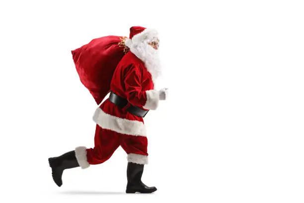 Full length profile shot of santa claus running with a sack on his shoulder isolated on white background