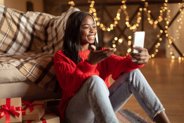 istock Cheerful black woman using mobile phone, making online video call, chatting with family on web on Christmas eve 1352852388