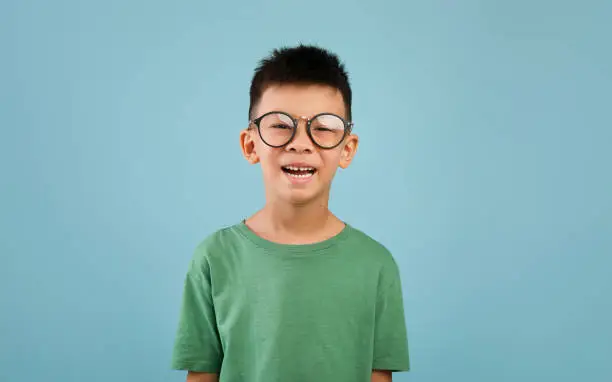 Photo of Portrait of cheerful little asian boy wearing eyeglasses posing over blue background