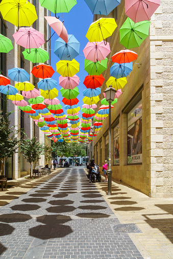 Jerusalem, Israel - August 30, 2021: Pedestrians and colorful umbrellas (parasols), in Yoel Moshe Solomon Street, the historic Nachalat Shiva neighborhood, the picturesque center of Jerusalem, Israel