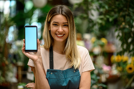Florist showing a smartphone while surrounded with flowers and plants in a flower shop