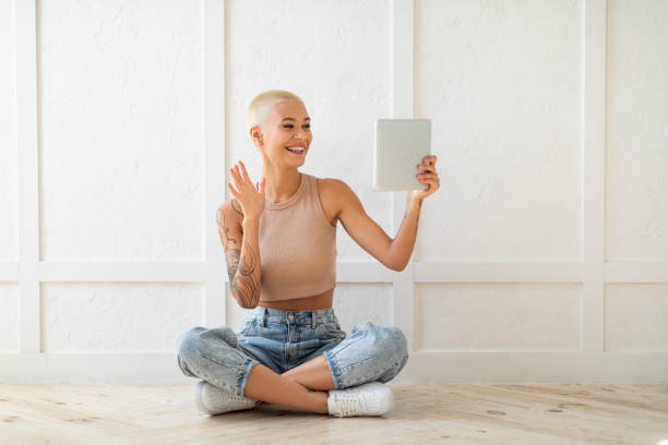 istock Modern communication concept. Young lady video calling via digital tablet, waving hand to webcam over white wall 1352853708