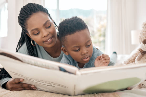 tiro cortado de um menino adorável e sua mãe lendo um livro em uma cama em casa - africa child reading african descent - fotografias e filmes do acervo