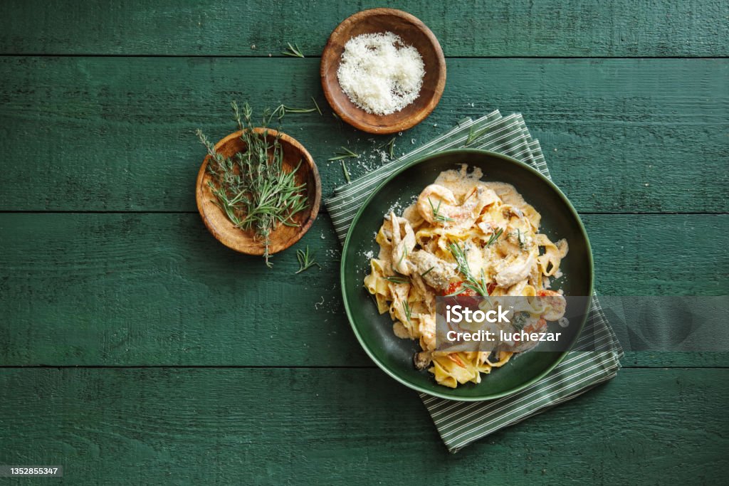 Italian Seafood Pasta Italian fettuccine with prawns, salmon and herbs. Flat lay top-down composition on dark green background. Food Stock Photo