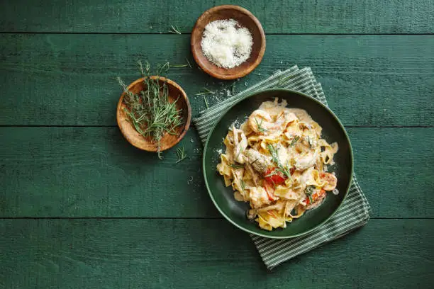 Italian fettuccine with prawns, salmon and herbs. Flat lay top-down composition on dark green background.