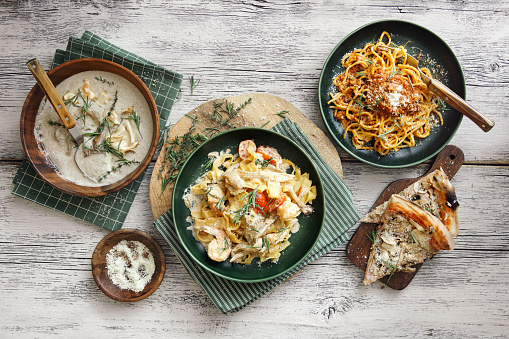 Classic spaghetti bolognese with parmesan cheese and herb. Italian fettuccine with prawns, salmon and herbs. Creamy wild mushroom soup with herb and vegetable chips. Beef-mushroom pizza. Flat lay top-down composition on wooden background.