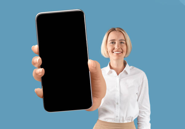 istock Smiling businesswoman showing smartphone with big blank empty screen at camera 1352856492