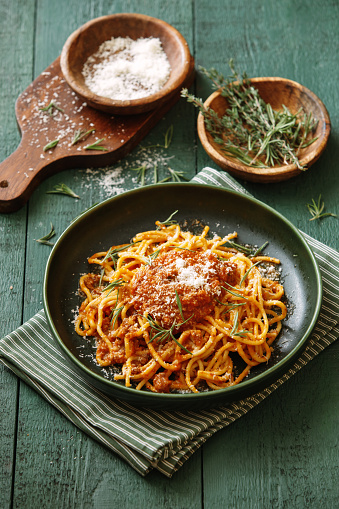 Classic spaghetti bolognese with parmesan cheese and herb. Close-up composition on dark green background.