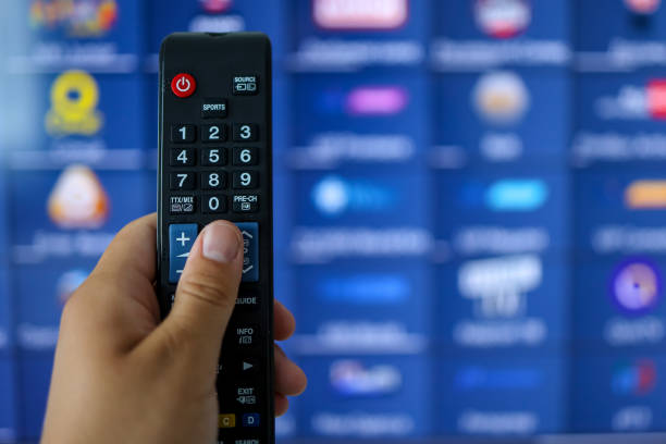 istock Smart tv and hand pressing remote control.Hand holding TV remote control with a television in the background. Close up. 1352856886