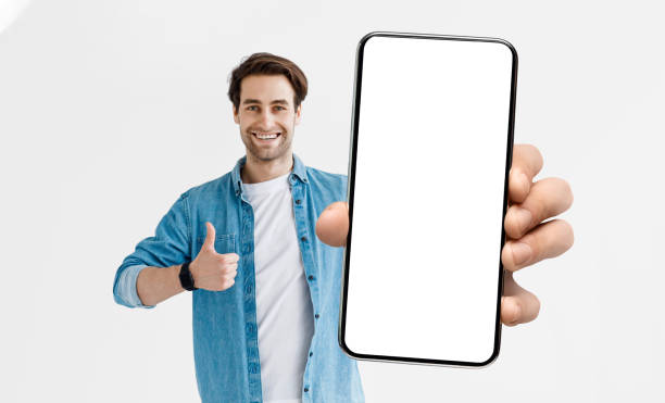 istock Cheerful Young Man Holding Smartphone With White Screen And Showing Thumb Up 1352856983