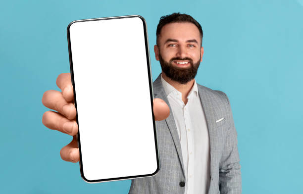 apuesto hombre de negocios árabe que muestra un teléfono inteligente con una gran pantalla blanca en blanco en la cámara - middle eastern ethnicity business men manager fotografías e imágenes de stock