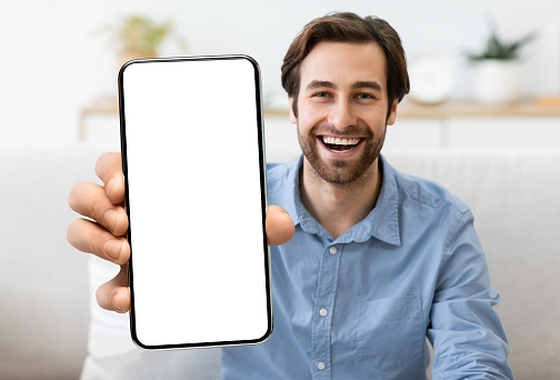 Joven emocionado demostrando un teléfono inteligente con una gran pantalla blanca en blanco en la cámara photo