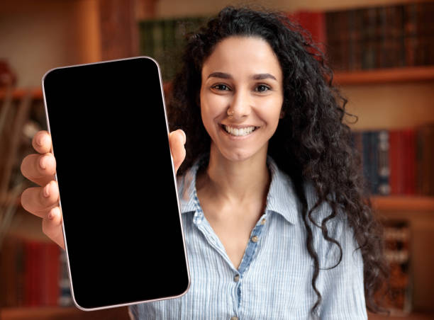 istock Online Offer. Young Smiling Lady Showing Blank Black Smartphone Screen At Camera 1352862088