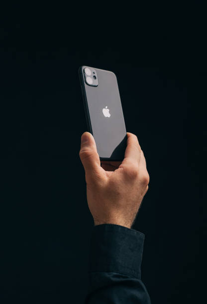 Male hand holds an iPhone 11 with apple logo on a black background. stock photo