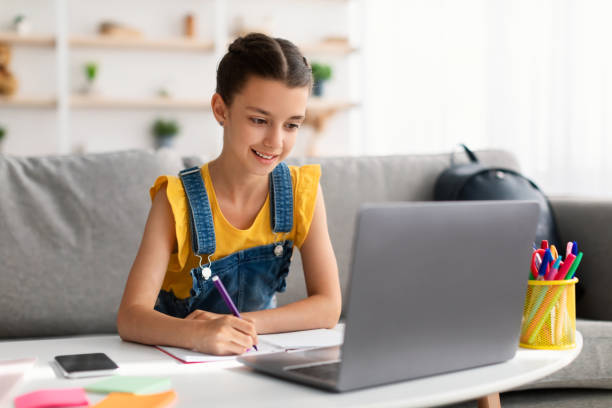 istock Cheerful teen sitting at desk, using laptop, drawing in copybook 1352866563