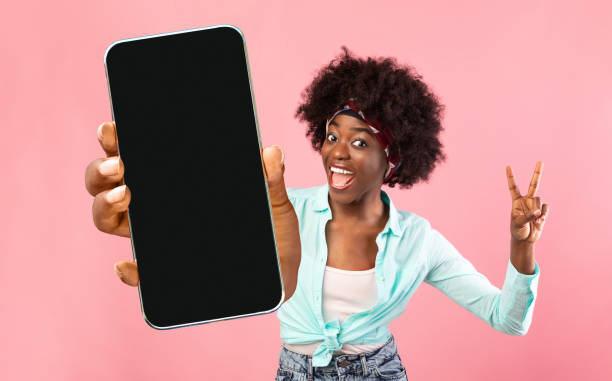 istock Great App. Black Woman Holding Smartphone With Blank Screen And Gesturing Peace 1352867298