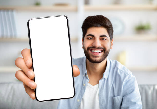 istock Cheerful Arab Man Showing Smartphone With Big Blank White Screen At Camera 1352867712