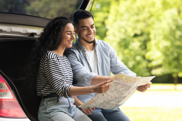 istock Happy lovers sitting on car trunk and watching map 1352867810