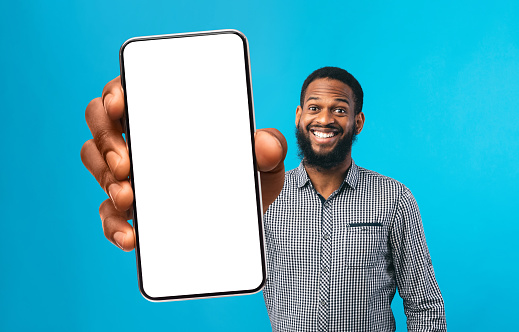 Cool Mobile App. Cheerful Black Man Showing Smartphone With Big White Screen, Funny African American Guy Demonstrating Copy Space For Your Design Or Advertisement, Standing On Blue Background, Mockup
