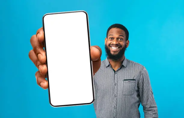 Photo of Cool Mobile App. Cheerful Black Man Showing Smartphone With Big White Screen