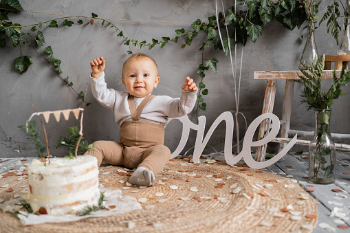 Happy birthday one year toddler, boy with cake sitting on the floor, natural background, rustic style decor, childrens birthday concept.