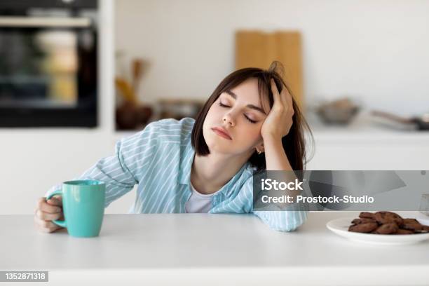 Sleepy Young Woman Drinking Coffee Feeling Tired Suffering From Insomnia And Sleeping Disorder Sitting In Kitchen Stock Photo - Download Image Now