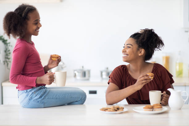istock Cheerful african american mom and daughter drinking tea with cupcakes 1352873588