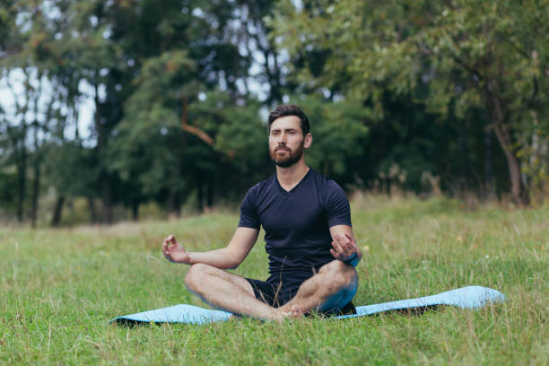 istock A young man with a beard sitting in the park on a mat meditates, performs exercises to improve breathing, active lifestyle 1352874857
