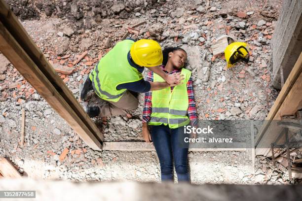 Construction Worker Giving First Aid To A Colleague Lying On His Back After An Accident Stock Photo - Download Image Now