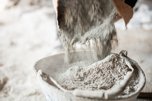 Close-up of a worker filling a bucket with cement from a bag at construction site.